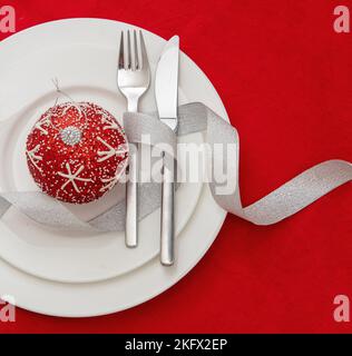 Christmas table setting. Xmas bauble and silver cutlery on plates, red background, top view. Holiday celebration dinner Stock Photo