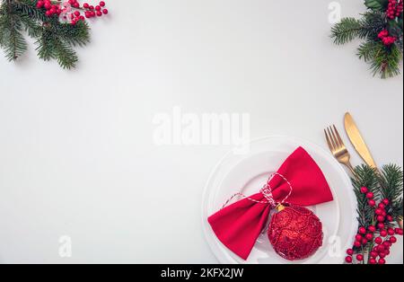 Christmas table setting, celebration dinner flat lay. Golden Cutlery, red cloth napkin and Xmas decoration on white background, top view, copy space Stock Photo