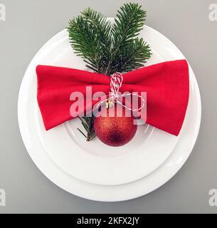Christmas table setting, celebration dinner. Red cloth napkin and Xmas decoration on white plates set, gray background, top view Stock Photo