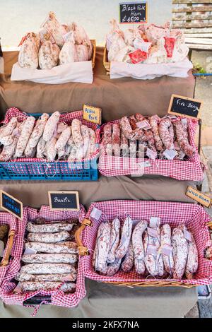 Close up of various types of French dried meat saucisson sec sausages, salami, in baskets for sale on an open air market stall. Stock Photo