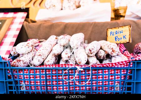 Red and white clothe with French dried meat saucisson sec sausages, salami, stacked up for sale on an open air market stall. Stock Photo