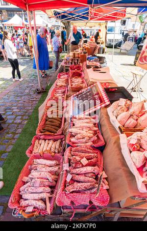 Various types of French dried meat saucisson sec sausages, salami, in baskets for sale on open air market stall. in background people and other stalls Stock Photo