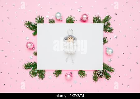 Christmas card. Princess on blank white paper in frame of natural fir tree branches and decorations on pastel pink flat lay background Stock Photo