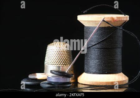 Spool of dark, black thread with needle and one metal thimble on white  background, home crafting, sewing kit, indoors, close-up Stock Photo - Alamy