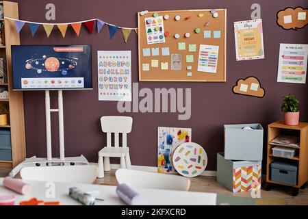Part of spacious classroom for primary school children with pictures and notes on boards, paintings, chair and boxes standing by wall Stock Photo
