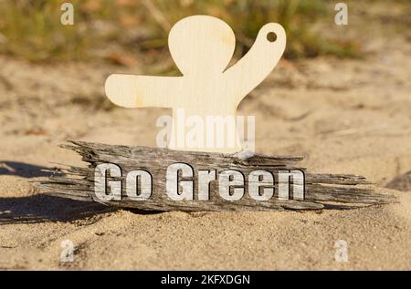 Ecology. On the sand near the wooden figurine of a man there is a piece of wood with the inscription - Go Green Stock Photo
