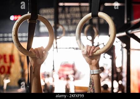 closeup tattooed hands and arms of young caucasian woman holding on to two large rings in a gym Stock Photo