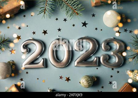 Numbers of year 2023 made by candles. Fir tree, gift box, holiday decoration on blue background. Christmas postcard. Happy New Year 2023 card concept. Stock Photo