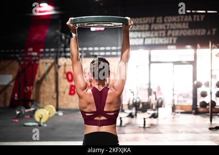 sporty caucasian girl on her back doing crossfit with a large round dumbbell on her head with her arms outstretched Stock Photo