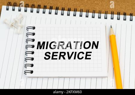 Business and economy concept. There are two notebooks and a pencil on the table. On the top notepad, the inscription - Migration Service Stock Photo
