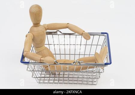 Business concept. The wooden man sits in a shopping basket. Isolated on white background. Stock Photo