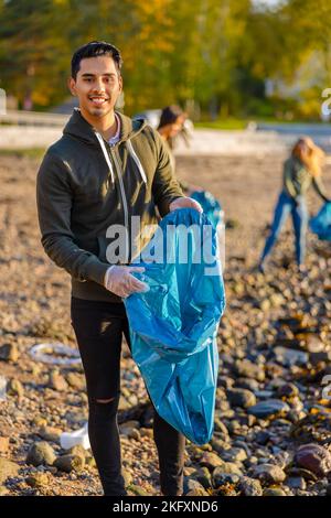 Young man collects garbage in bag with group of volunteers on sunny day Stock Photo