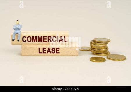 Business concept. On the table are coins, wooden plates with the inscription - COMMERCIAL LEASE. A figure of a businessman sits on the dice. Stock Photo