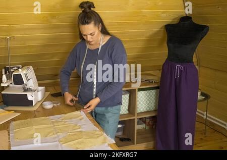 The fashion designer cuts the fabric according to patterns with scissors. Small business. Stock Photo