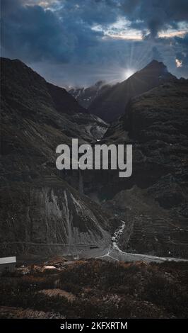 A vertical panoramic of the sun rising behind tall mountains of India and a small river coming through them Stock Photo