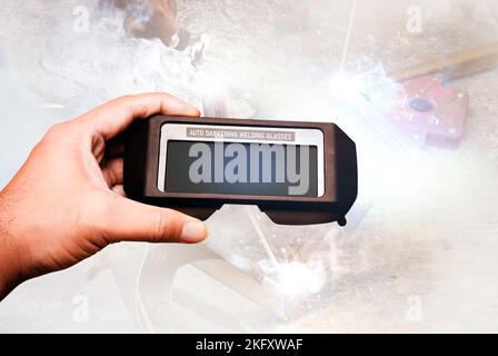 Auto darkening welding glasses in the mechanic hand with a welding on background,Double exposure welding tools concept Stock Photo