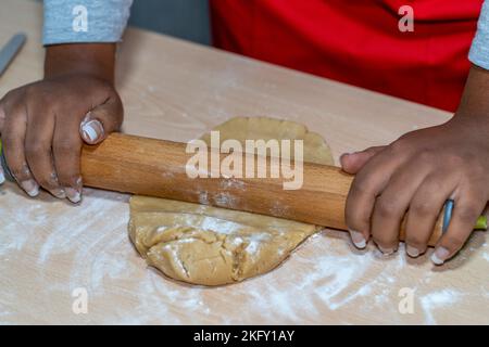 young woman kneading with a rolling pin the dough of cinnamon and vanilla biscuits Stock Photo