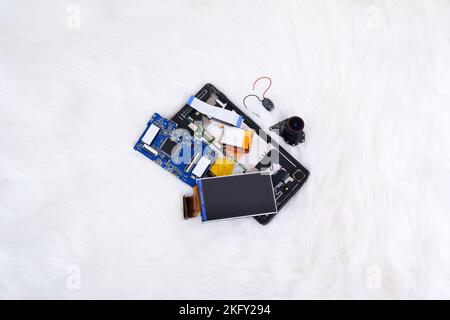 Electronics waste including a lcd screen,a electronic board,a battery,a camera lens and smartphone on white fur rug background Stock Photo