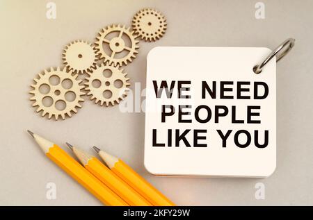 Business and finance concept. On the table are gears, pencils and a notebook with the inscription - We Need People Like You Stock Photo