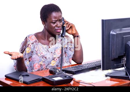 beautiful angry young businesswoman talking on mobile phone at the office while looking at the laptop. Stock Photo