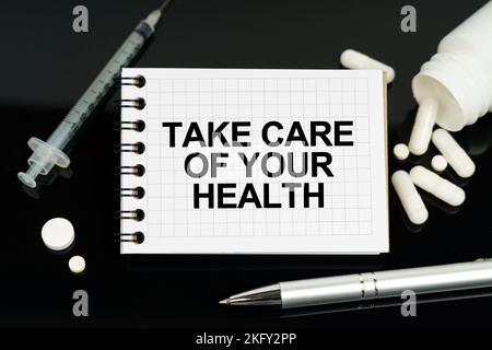 Medicine and healthcare concept. On the black surface are pills, a syringe and a notebook with the inscription - Take care of your health Stock Photo
