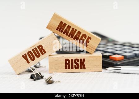 Business and Economics. On the table is a pen, a calculator and small wooden blocks with the inscription - Manage Your Risk Stock Photo