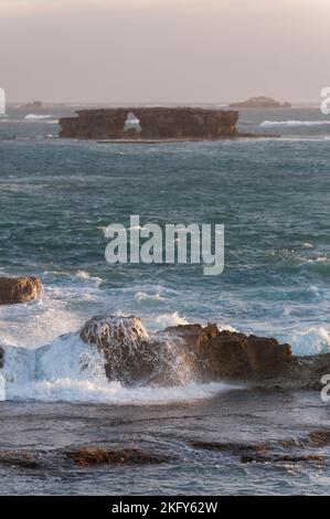 Rough seas in the late afternoon highlight the waves crashing over reefs and the archway in doorway rock beyond that make these waters so treacherous Stock Photo