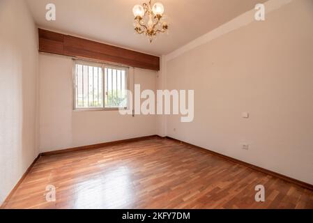 Empty living room with reddish parquet with matching skirting boards and wooden doors with aluminum barred windows and multi-arm ceiling lamp Stock Photo