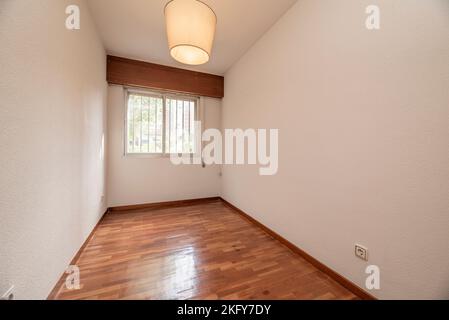Empty living room with reddish parquet flooring with matching skirting boards and wooden doors with aluminum barred windows Stock Photo