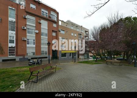 Facades of residential buildings on a rainy day seen from a square with trees, cement paver floors and wooden seats Stock Photo