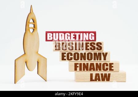 Business and finance concept. On the white surface there is a wooden rocket and planks, on the red plaque the inscription - BUDGETING Stock Photo