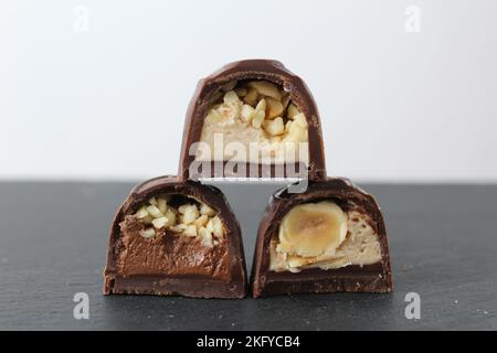 three chocolate glazed case candies with praline chocolate filling and nuts whole and crushed peanuts and hazelnuts lie pyramidally on top of each oth Stock Photo