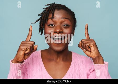 African american happy woman smiling and pointing at copyspace isolated over blue background Stock Photo