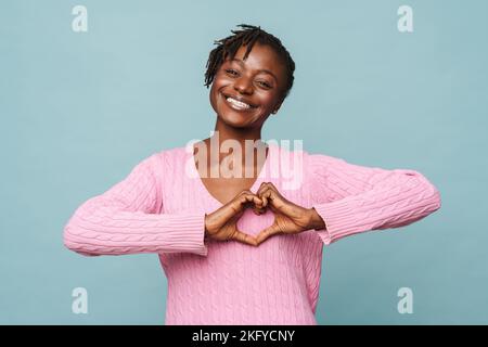 African american happy woman smiling and gesturing heart-shape sign isolated over blue background Stock Photo