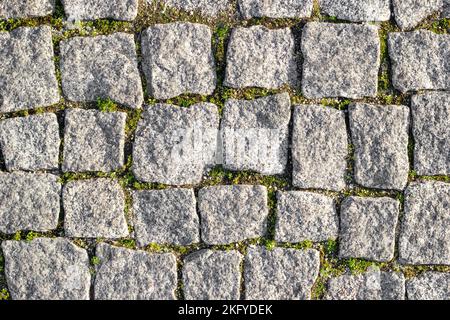 Stone road paved with asymmetrical stones with sprouted grass between stones. Textured background, top view Stock Photo