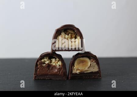 three chocolate glazed case candies with praline chocolate filling and nuts whole and crushed peanuts and hazelnuts lie pyramidally on top of each oth Stock Photo