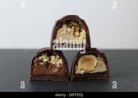 three chocolate glazed case candies with praline chocolate filling and nuts whole and crushed peanuts and hazelnuts lie pyramidally on top of each oth Stock Photo
