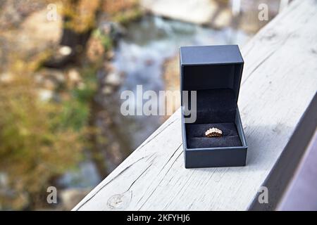 Diamond Ring set in yellow gold in a black box sitting on a wooden railing outdoors Stock Photo