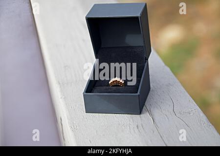 Diamond Ring set in yellow gold in a black box sitting on a wooden railing outdoors Stock Photo
