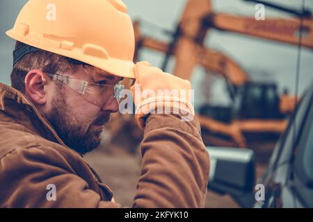 Closeup of Professional Construction Worker Wearing Yellow Hard Hat, Protective Glasses and Gloves. Industrial Safety Equipment Theme. Stock Photo