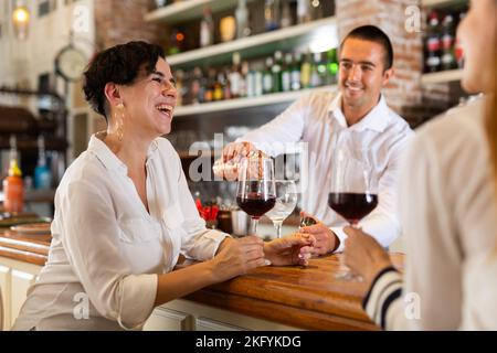 Two girlfriends chat with each other and drink red wine while sitting at bar in restaurant Stock Photo