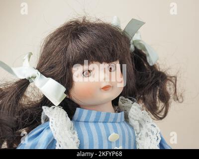 Garham, Germany. 18th Nov, 2022. In this photo illustration, a vintage porcelain doll girl with brown eyes brunette with braided ribbons in a blue dress with white vertical stripes and a lace apron. Porcelain dolls appeared in the 18th century in France. They were used to promote French fashion in the world. Usually such dolls were supplied with a large number of clothes and sent to customers as mini mannequins. (Credit Image: © Igor Golovniov/SOPA Images via ZUMA Press Wire) Stock Photo