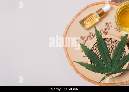 Set of legalized marijuana includes green hemp leaf, CBD oil in a bottle with a dropper lid and a glass bowl, and hemp seed displayed on a wooden Stock Photo