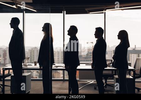 Silhouette photo of a group of businessmen standing side by side in profile in office Stock Photo