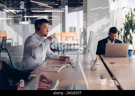 Focused asian businessman drinking coffee while working on computer in modern office Stock Photo