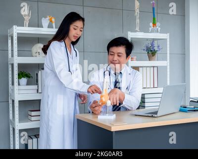 Two Asian doctors in white uniforms talking and working together in medical office. The adult male doctor counseling to young female doctor about the Stock Photo