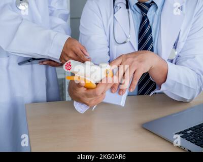 The knee ligaments model holding and pointing by doctor's hands, counseling by adult male specialist to young female doctor with tablet. Two doctors t Stock Photo