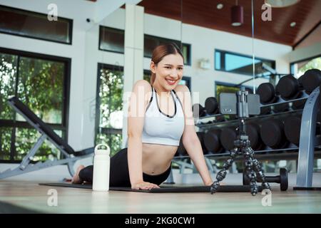 Young woman watching fitness video or having video conference with fitness trainer at smartphone screen. Stock Photo