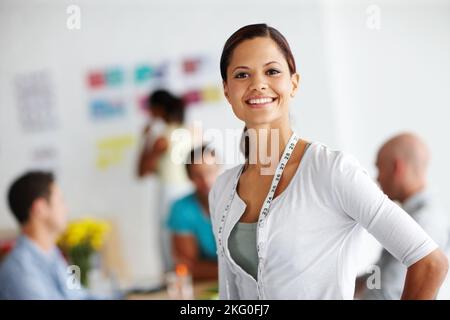 They use old and new technology in their designs. Portrait of a confident-looking young woman with a tape measure around her neck and colleagues Stock Photo