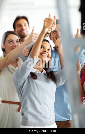 Showing their approval. A group of colleagues looking up and showing thumbs up to someone on a ladder. Stock Photo